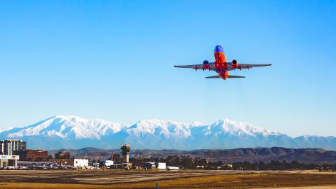 Plane taking off from John Wayne Airport with snowy mountains in background